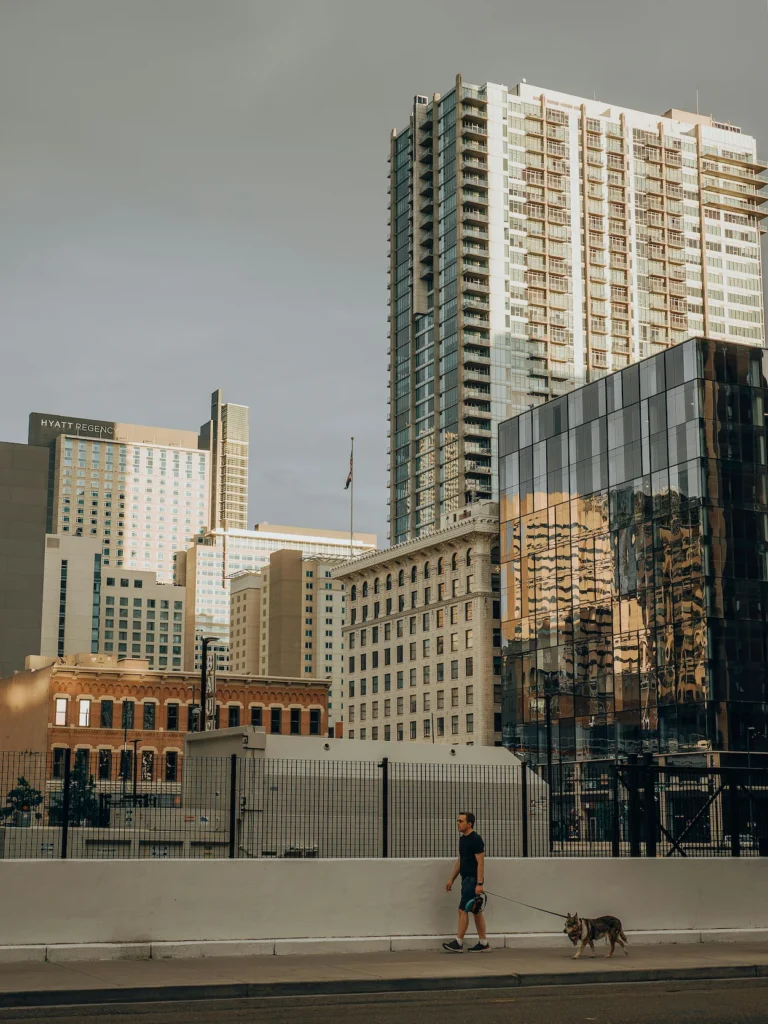 Man walking a dog past modern skyscrapers and the Hyatt Regency hotel in downtown Denver, Colorado