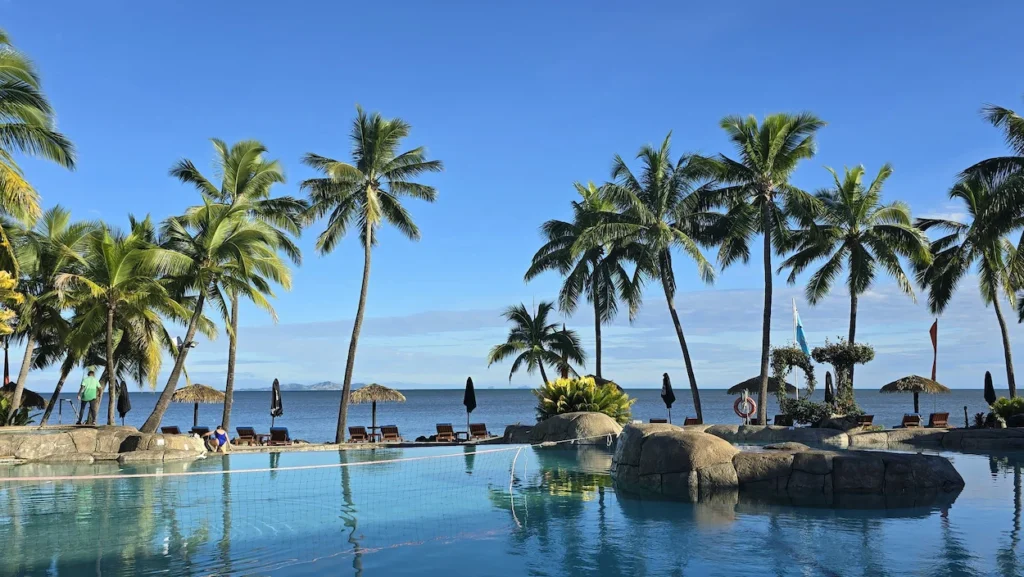 Fiji beach resort infinity pool featuring a volleyball net and palm trees facing the ocean