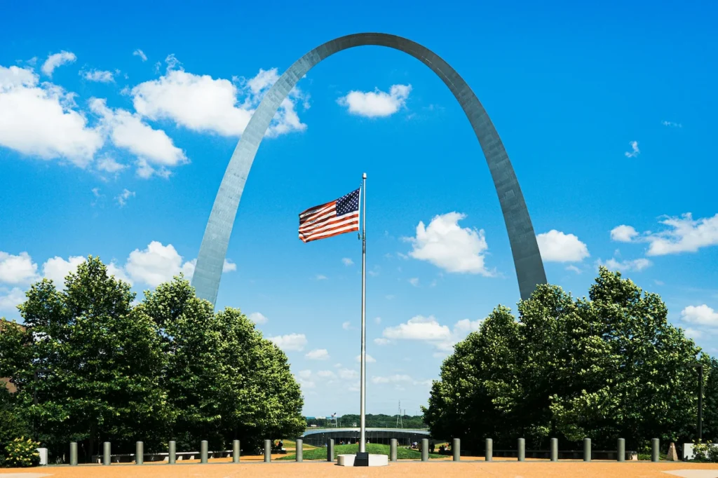 The Gateway Arch behind an American flag at Gateway Arch National Park in St. Louis