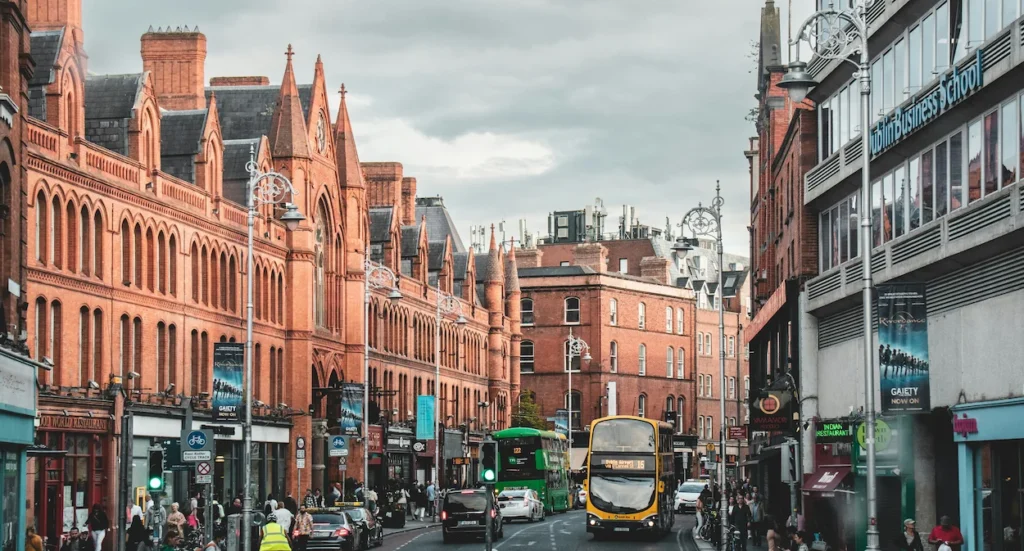 Busy Dublin street with red brick buildings, double-decker buses, and streetlights