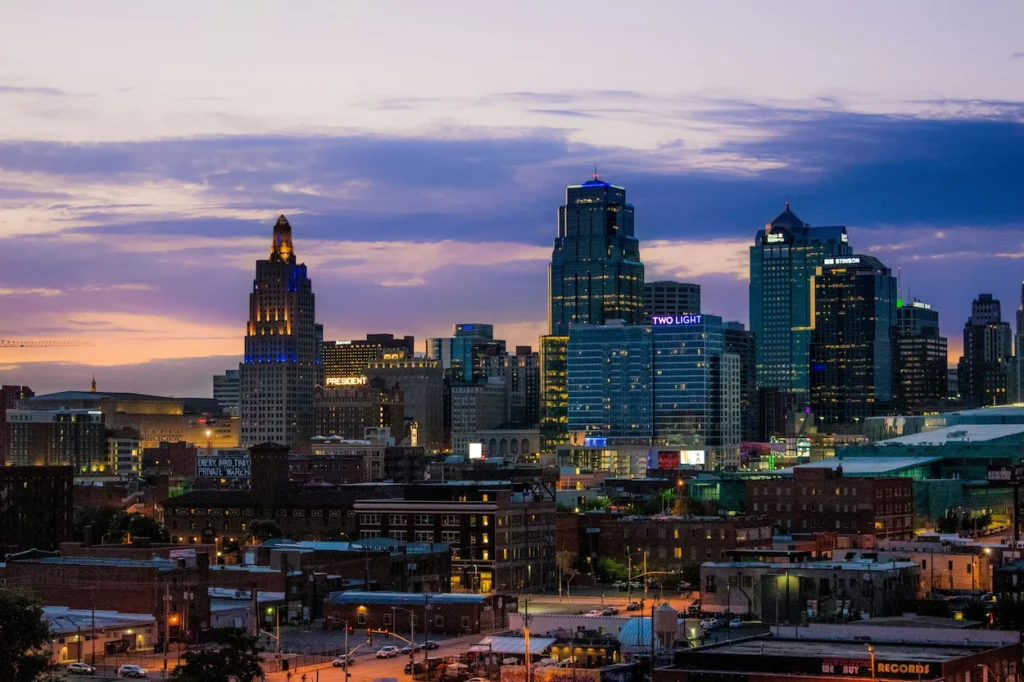 Kansas City downtown skyline at twilight with lit skyscrapers under a purple and orange sunset sky