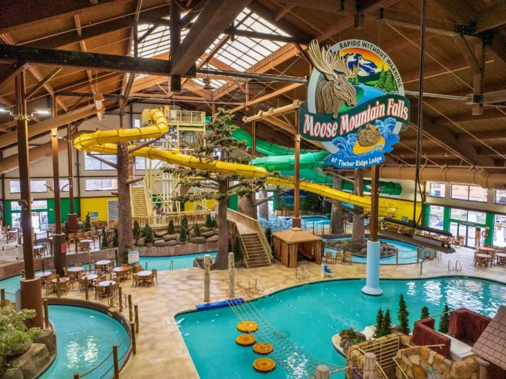 An indoor waterpark with large yellow and green slides, a swimming pool, and a Moose Mountain Falls sign