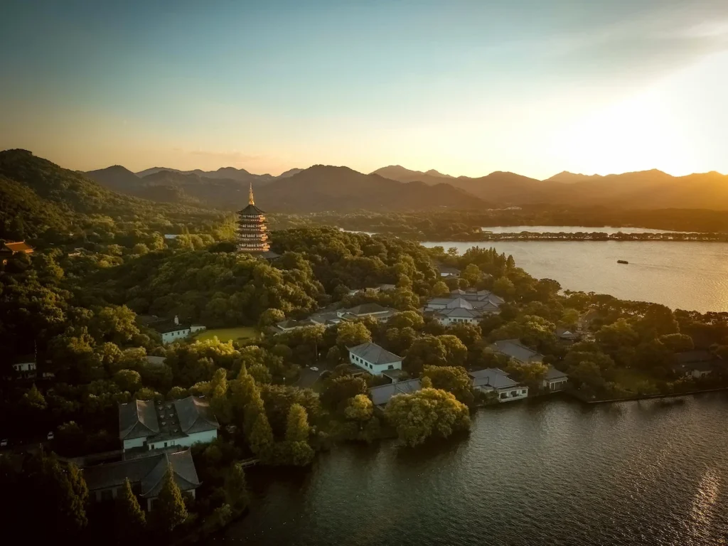 Aerial sunset view of Leifeng Pagoda on a forested hill next to West Lake in Hangzhou