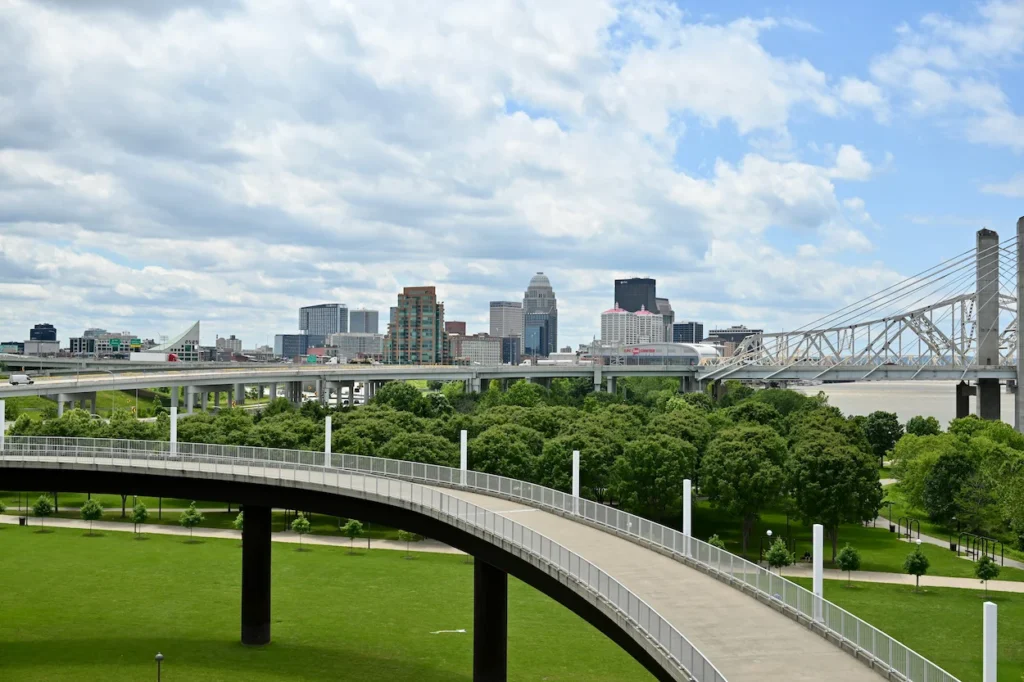 Curved elevated ramp over green park lawns with the Louisville skyline behind