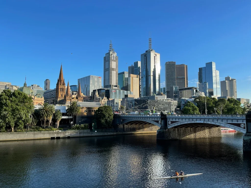 The Melbourne city skyline and Princes Bridge overlook a rower on the Yarra River