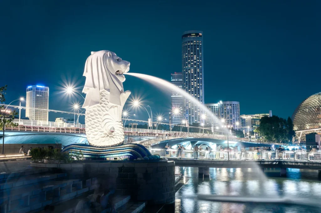 The illuminated Merlion statue spouting water into Marina Bay at night
