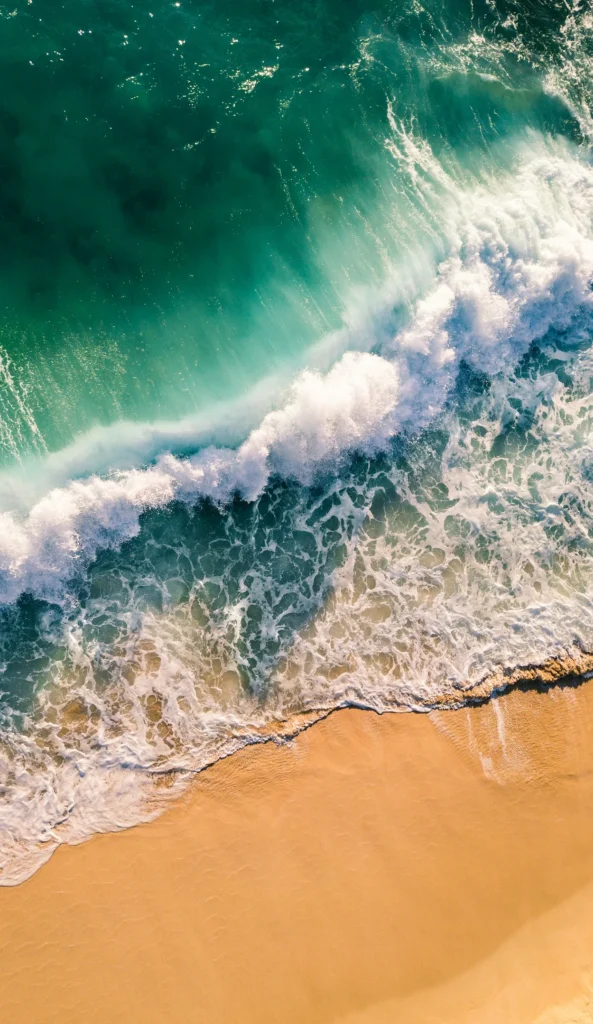 Aerial view of a turquoise ocean wave crashing onto the sandy North Shore beach in Oahu, Hawaii