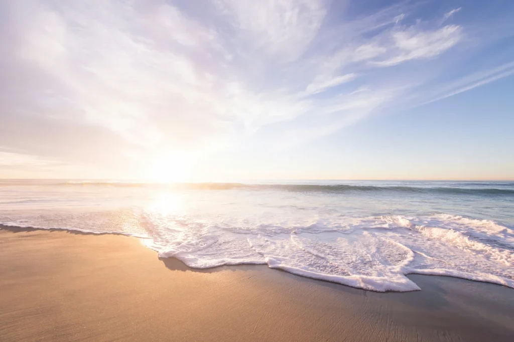 Ocean waves crashing onto a sandy beach under a bright sunrise
