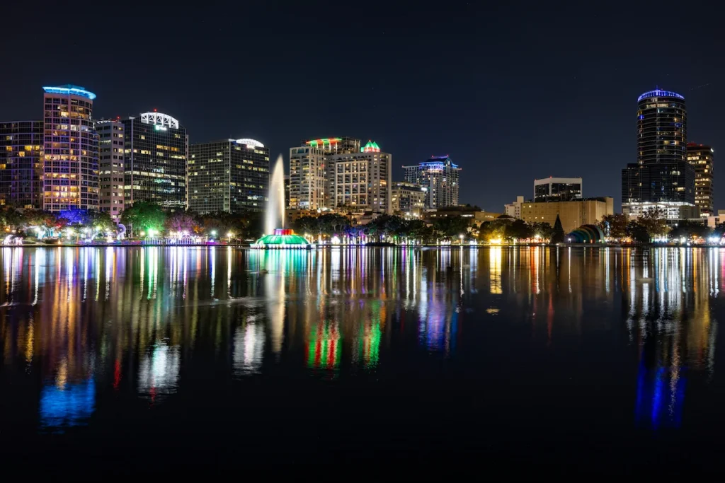 Illuminated skyscrapers and a colorful fountain reflected on Lake Eola at night in Orlando, Florida