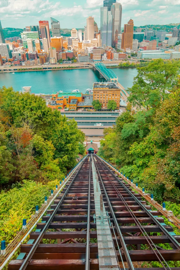 Looking straight down a steep funicular railway track toward a river and city skyscrapers