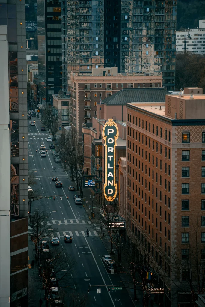 Vertical neon Portland sign hanging over Broadway Street surrounded by downtown city buildings