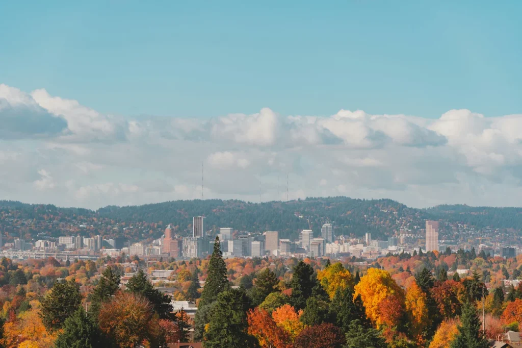 Portland skyline nestled behind dense green, orange, and yellow fall trees under puffy clouds