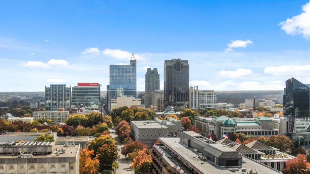 Downtown Raleigh high-rise buildings and autumn trees under a bright blue sky