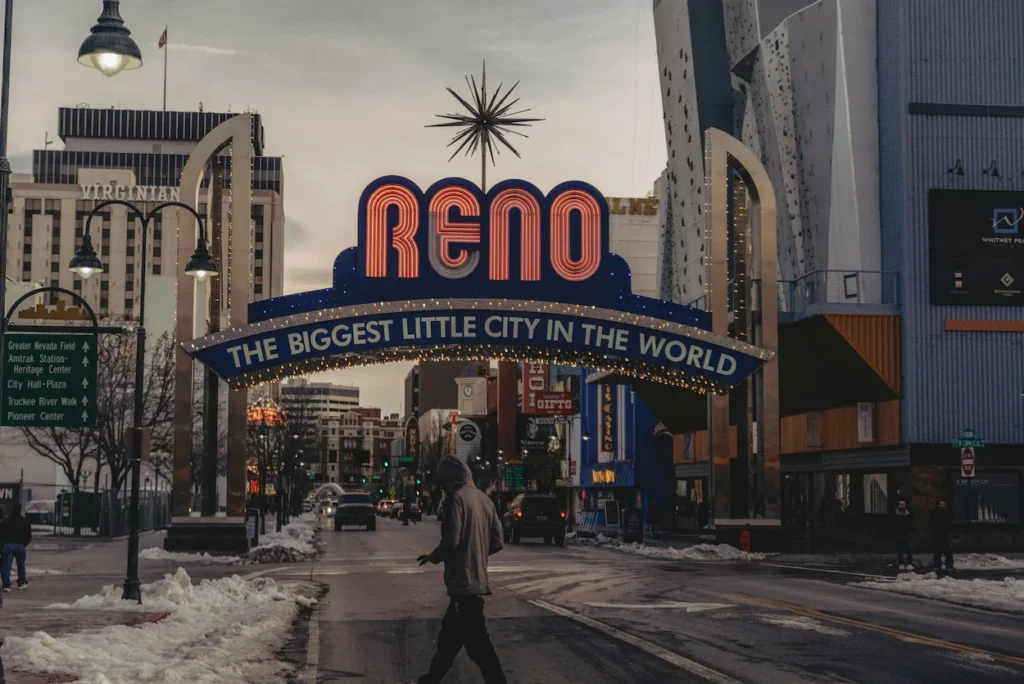Reno Arch sign lit up over a city street during twilight with light snow on the ground