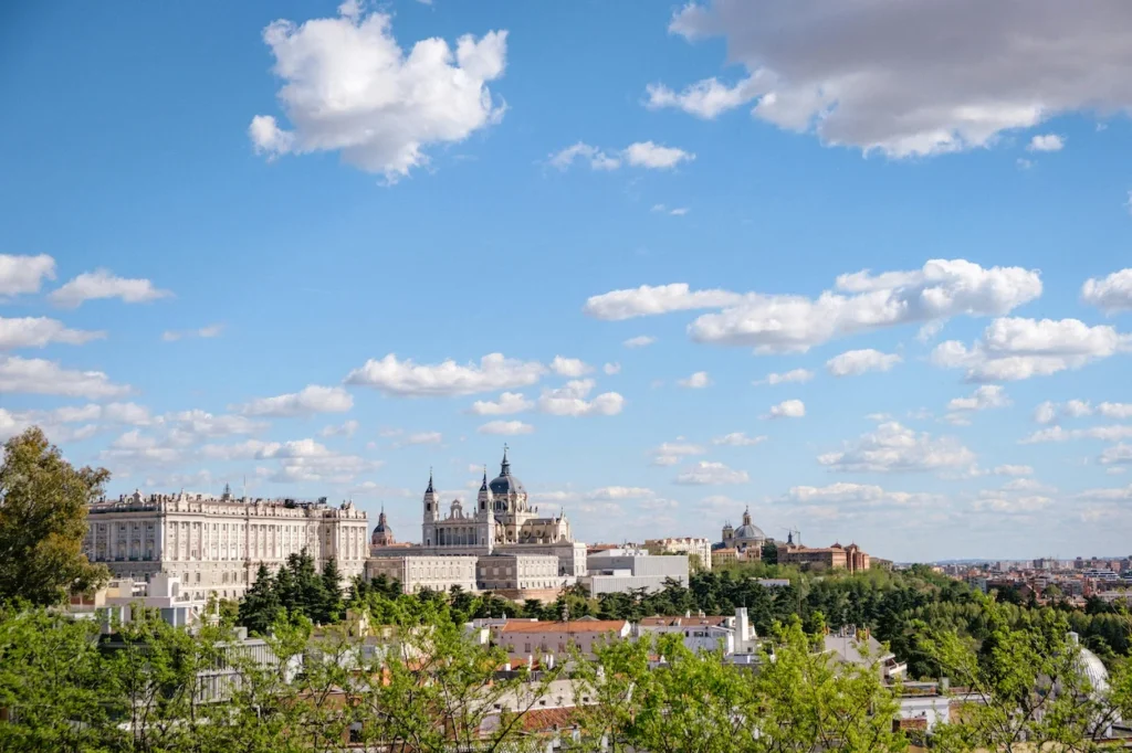 Wide skyline view of the Royal Palace of Madrid and Almudena Cathedral under a cloudy blue sky