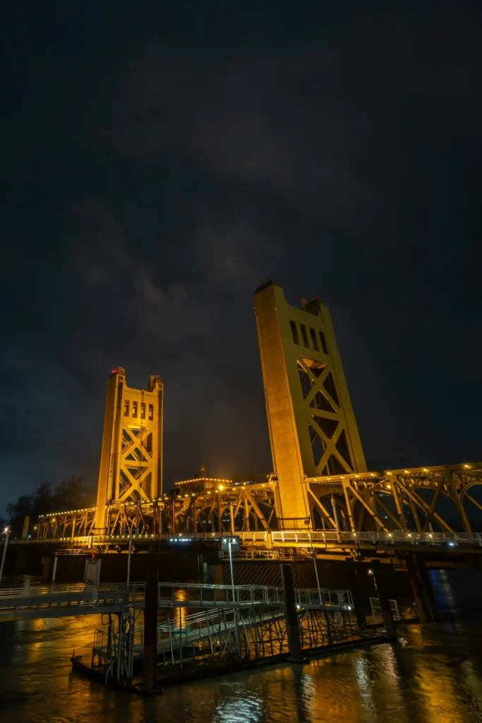 Gold illuminated Tower Bridge at night over the river under a dark, cloudy sky
