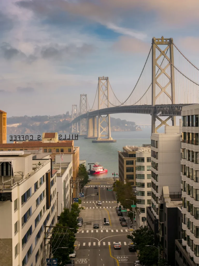 Looking down Harrison Street toward a red fireboat on the water framed by the San Francisco-Oakland Bay Bridge