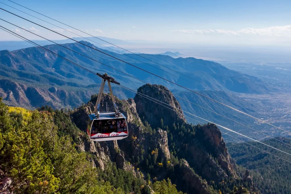 A passenger tram car suspended on cables high above the rugged Sandia Mountains