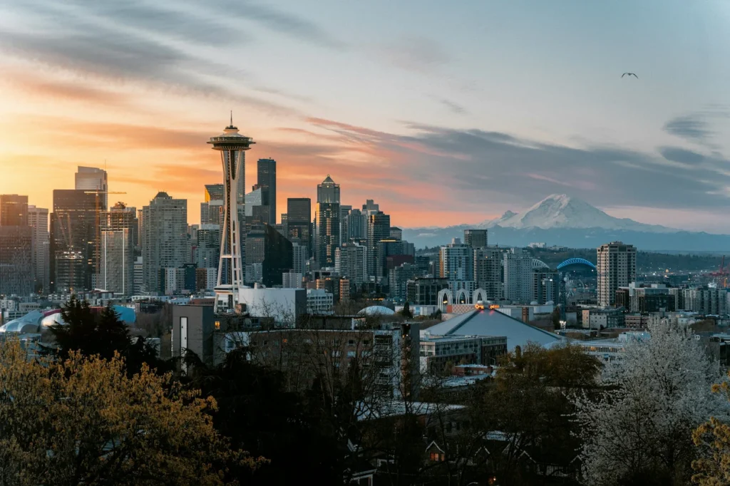 Seattle skyline at sunset featuring the Space Needle and a snow-capped Mount Rainier in the distance