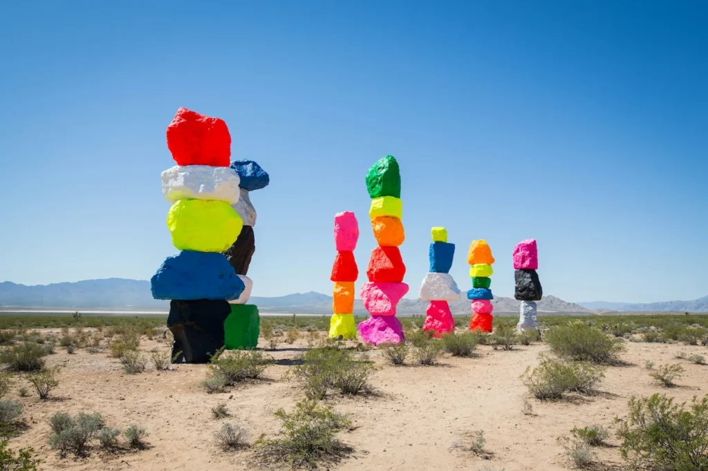 Seven tall towers of stacked, brightly painted neon boulders standing in the open Nevada desert near Las Vegas