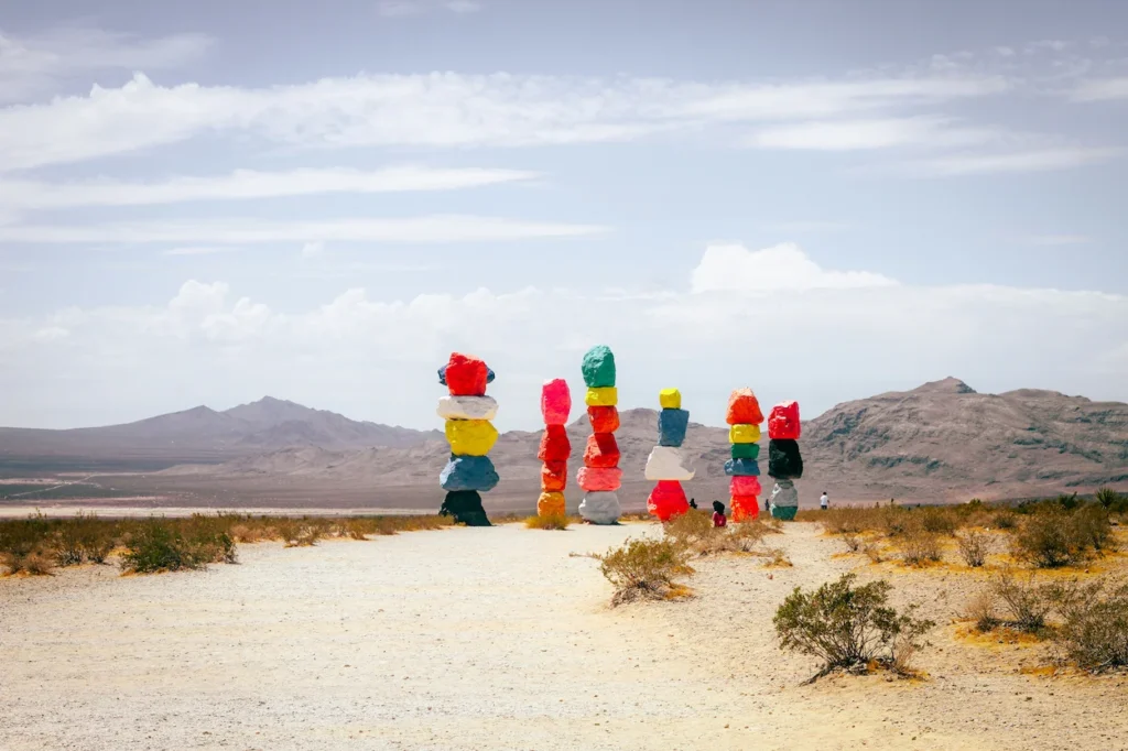 Seven tall towers of brightly painted, stacked boulders standing in the Nevada desert under a partly cloudy sky