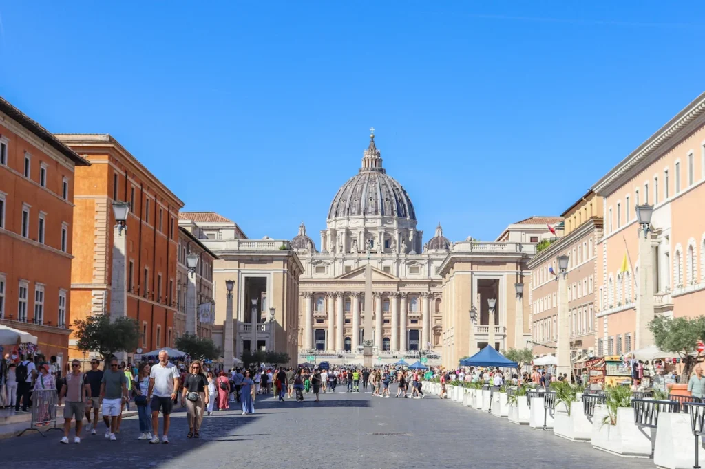 St. Peter's Basilica dome viewed down the crowded Via della Conciliazione street under a clear blue sky