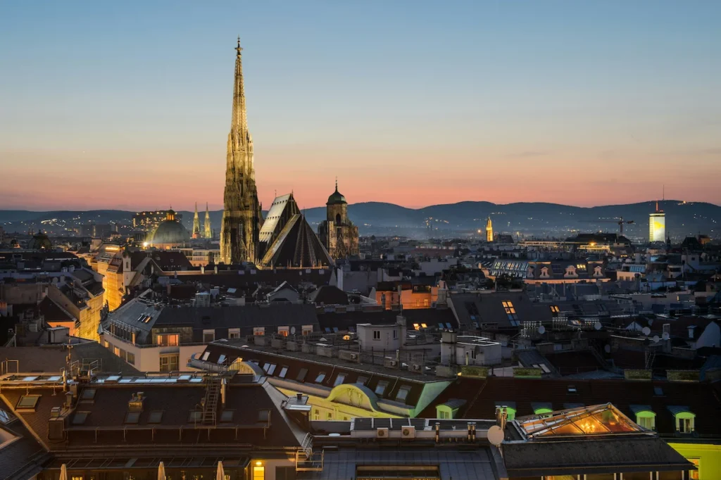Illuminated spire of St. Stephen's Cathedral rising above the Vienna city skyline at dusk