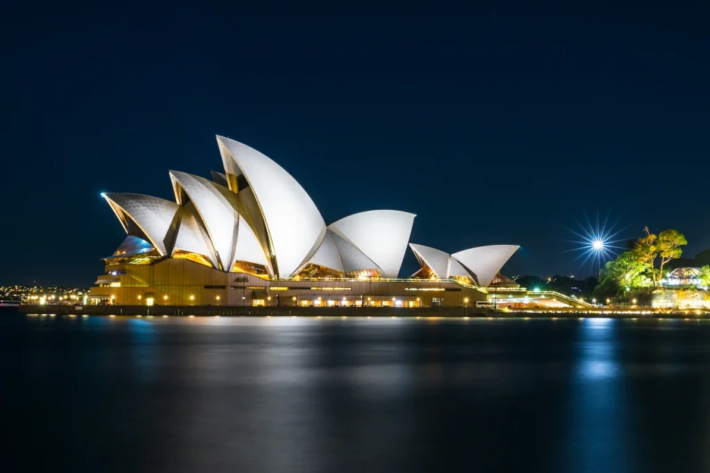 The brightly illuminated sails of the Sydney Opera House reflecting on the dark harbor waters at night
