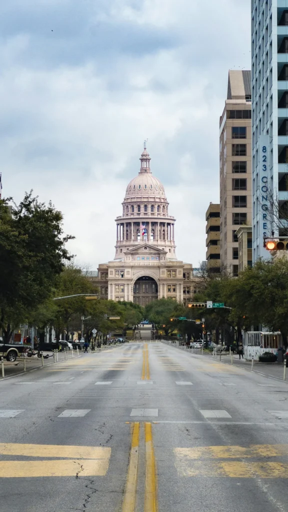 Texas State Capitol building centered at the end of an empty Congress Avenue street under a cloudy sky