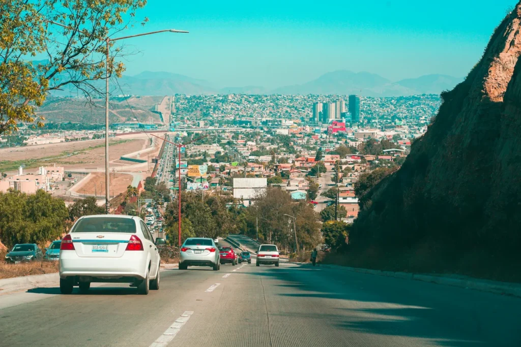 Cars driving downhill toward the sprawling city of Tijuana, Mexico, with the border wall visible on the left