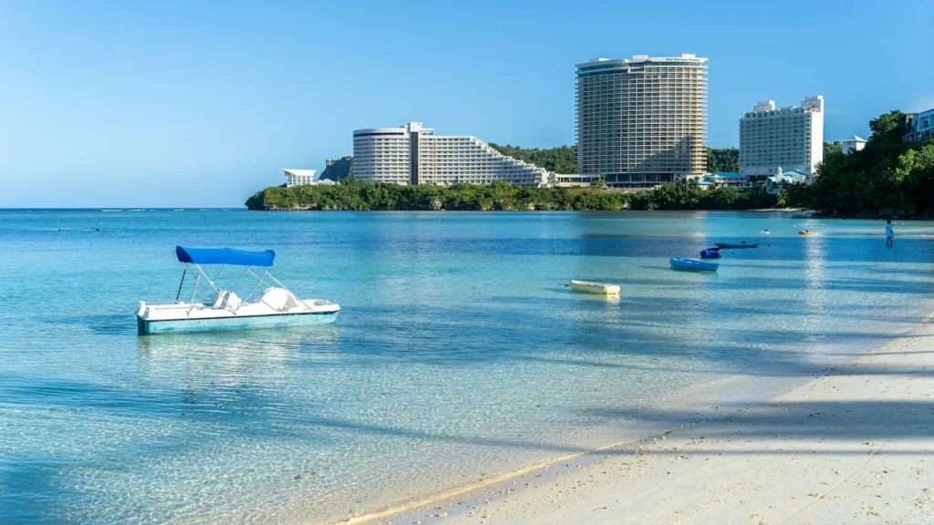 Tumon Bay beach in Guam with a blue paddle boat floating in clear water near shore hotels
