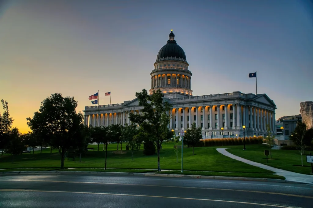 The lit Utah State Capitol building sitting on a green hill during twilight