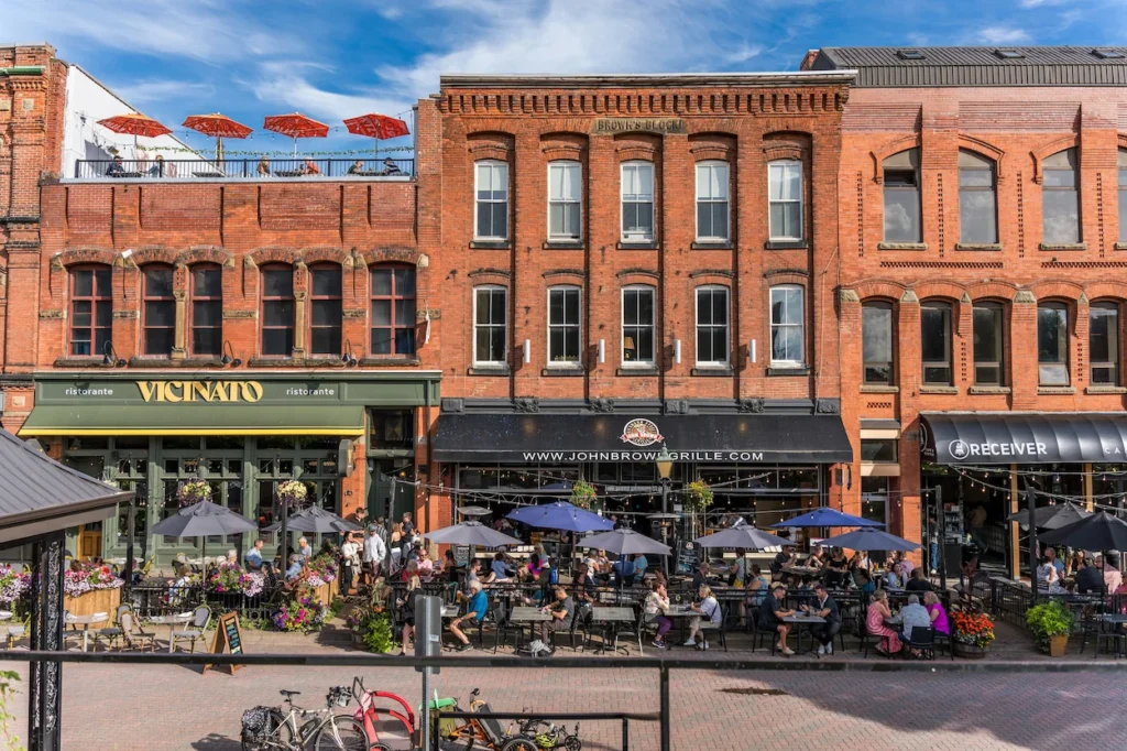 Patrons dining at outdoor tables under umbrellas along a historic brick building row in Charlottetown