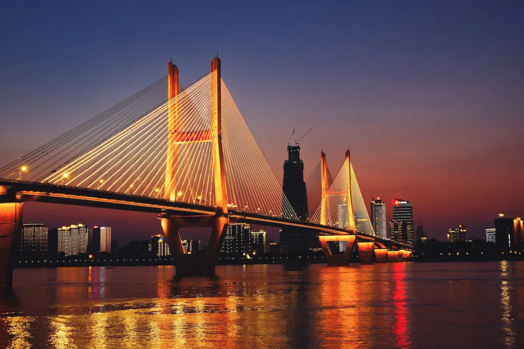 Erqi Yangtze River Bridge illuminated at sunset with city skyscrapers in the background