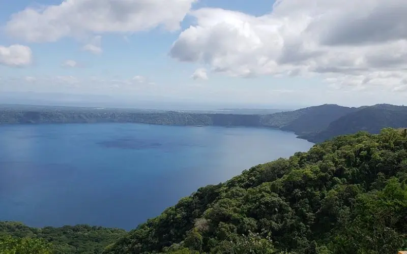 View of Apoyo Lake surrounded by green hills under a cloudy sky.