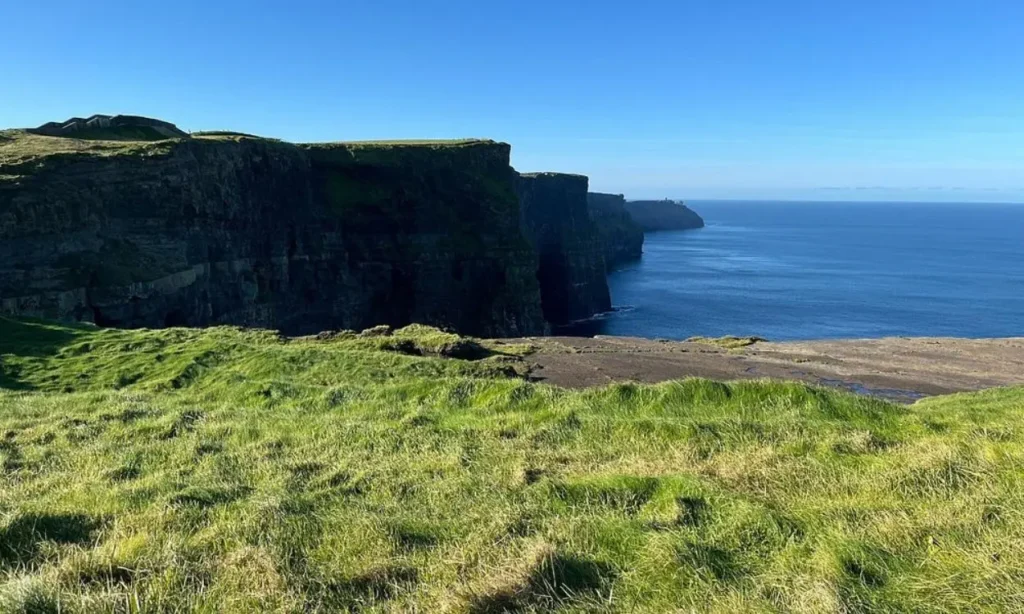 The Cliffs of Moher rise dramatically above the Atlantic Ocean under a clear blue sky.