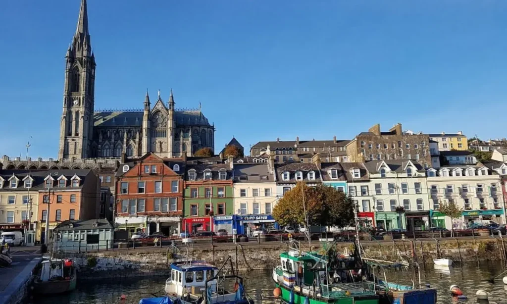 Cobh displays colorful waterfront buildings with boats in the harbor and a large cathedral in the background.