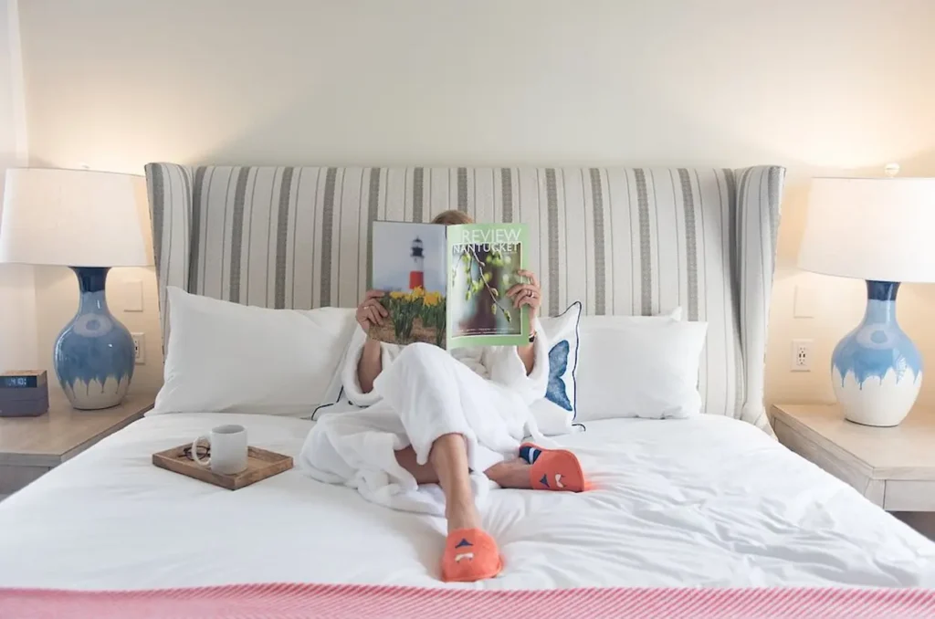 A woman reading a magazine in bed at The Nantucket Hotel & Resort