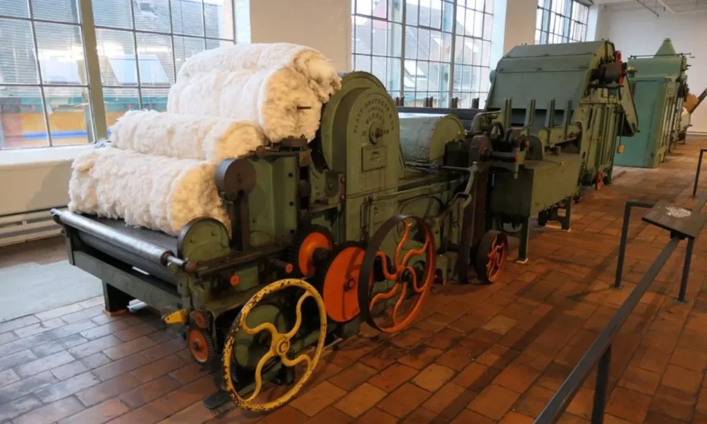 Museum of Industry (MIAT) with old textile machinery and cotton on display inside a brick-floored hall.