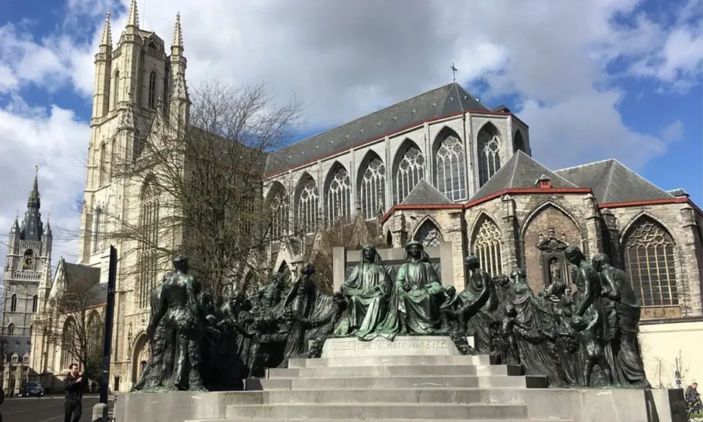 St. Bavo's Cathedral with a bronze monument in front and a cloudy sky above.