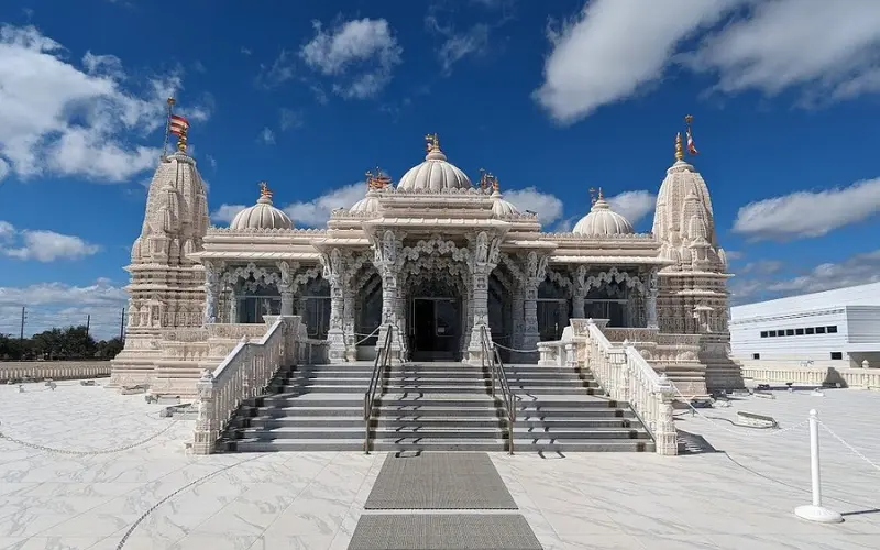 White marble architecture of BAPS Shri Swaminarayan Mandir under a blue sky.
