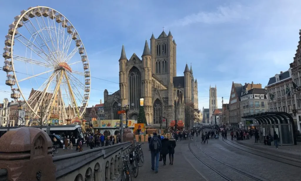 A lively Korenmarkt square with a Ferris wheel, a large church, and people walking.