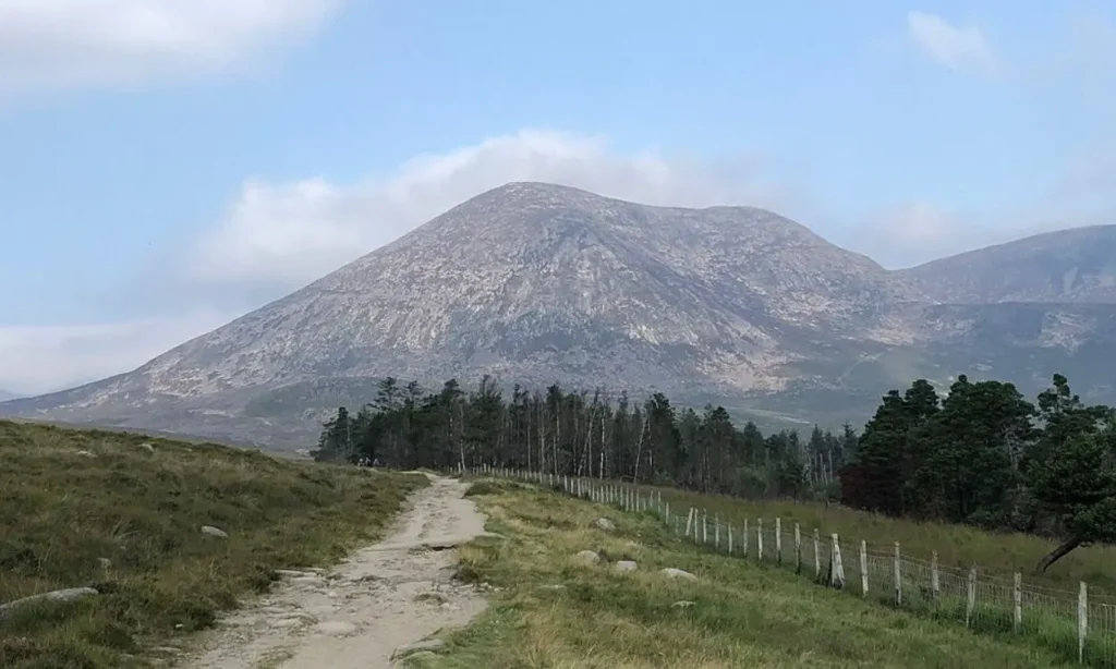 The Mourne Mountains feature a rocky peak with a dirt trail leading through open fields.
