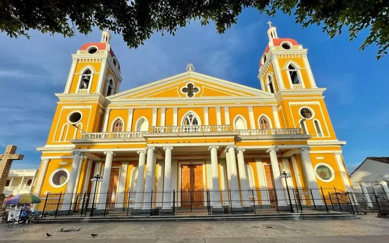 Bright yellow Granada Cathedral with two towers and white columns.