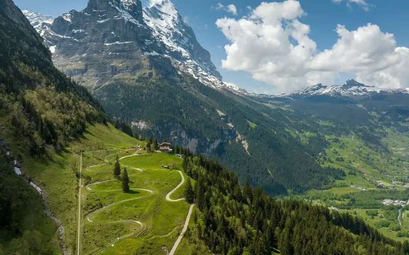 The Pfingstegg Toboggan Run winds down a grassy hillside below the mountains.