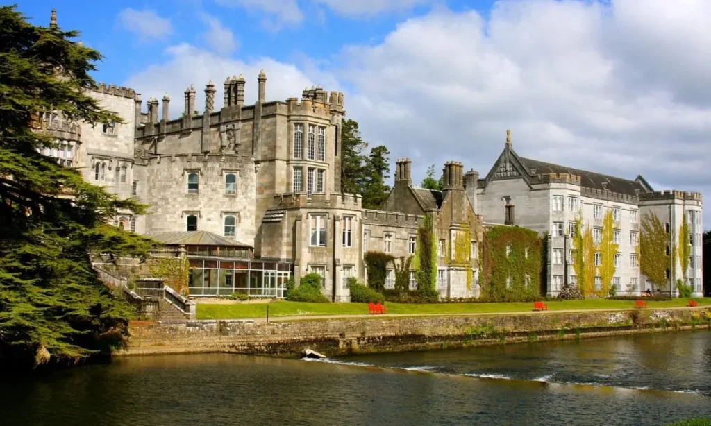 Adare Manor sits beside a calm river with stone architecture and ivy-covered walls.