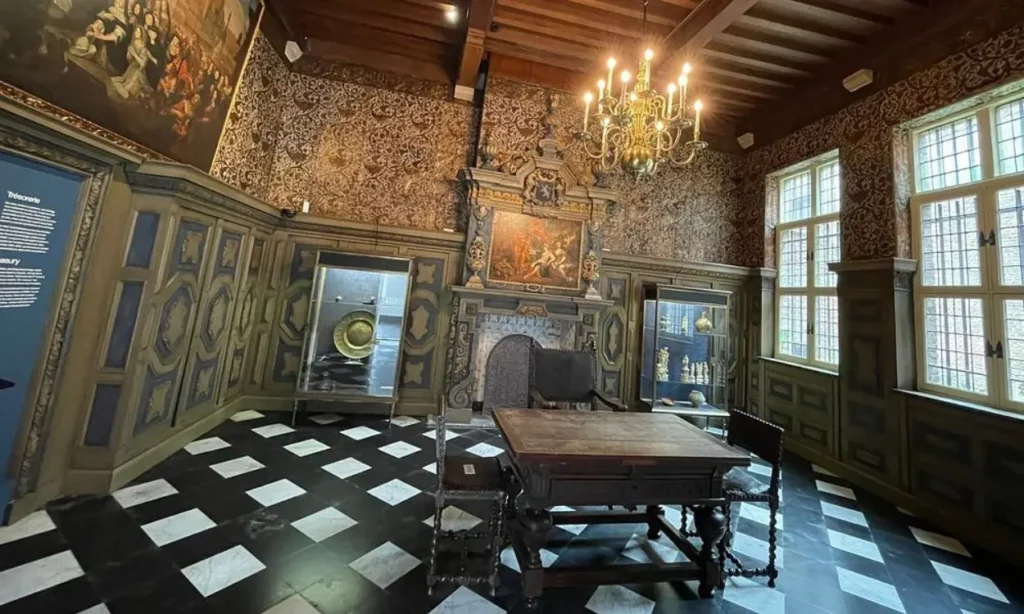 An ornate room in Ghent City Museum (STAM) with antique furniture, chandeliers, and display cases.