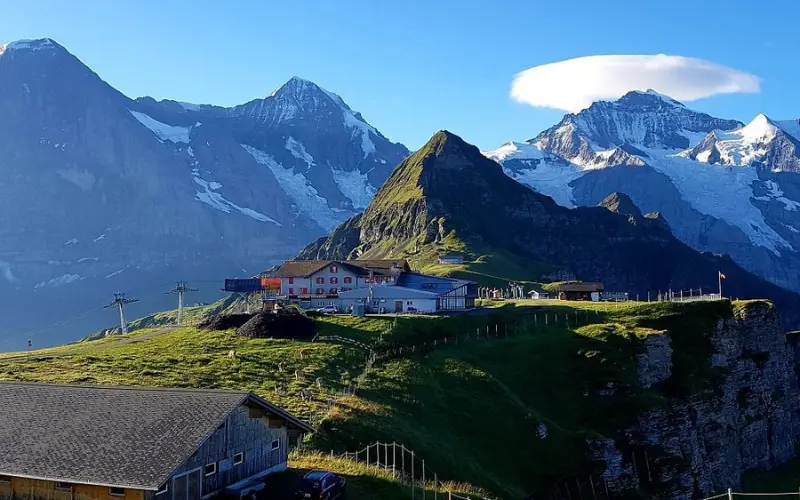 Mountain huts sit on the slopes of Männlichen with snowy peaks in the distance.