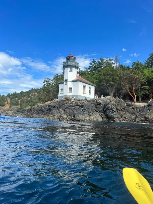 Kayaker paddling near a rocky shoreline with a lighthouse using Discovery Sea Kayaks.