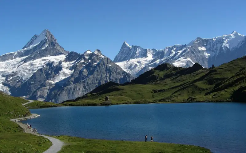 The calm blue waters of Bachalpsee reflect snowy alpine mountains under a clear sky.